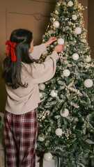 Young woman decorates a festive Christmas tree with white ornaments and warm lights