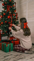 Woman decorating a Christmas tree with red ornaments and ribbons, surrounded by gifts