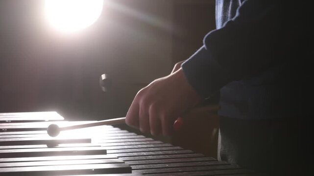 A close-up of a man playing the xylophone in silhouette in a concert hall. A teacher demonstrates how to play percussion instruments, percussion against the spotlight.