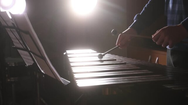 A close-up of a man playing the xylophone in silhouette in a concert hall. A teacher demonstrates how to play percussion instruments, percussion against the spotlight.