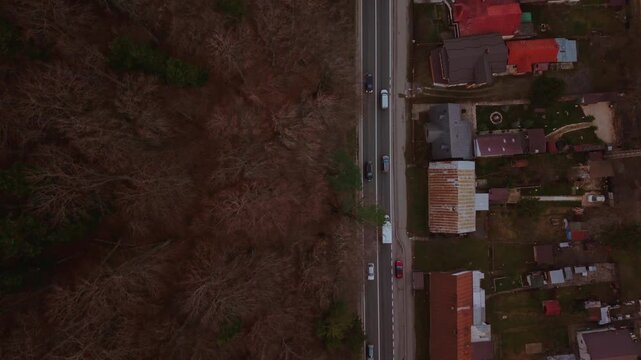Top down aerial drone footage of the DN1 road crossing Busteni town, showing traffic flow between forest and residential areas during winter daylight in Busteni, Romania.