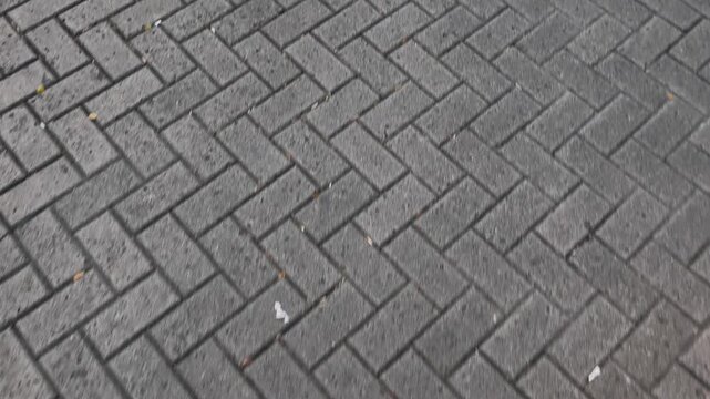 Top-down video features a close-up, moving shot of a herringbone pattern brick pavement and the shadows of people walking. 4k 60 fps. 3840 x 2160.