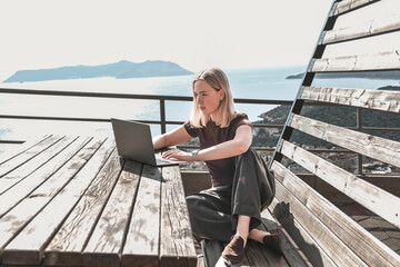 Digital nomad working on laptop on scenic terrace with sea view, remote work, workation lifestyle,...