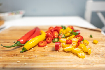 Sliced and whole chili peppers arranged on a wooden cutting board with soft background blur. Colorful spicy food concept.