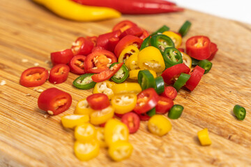 Fresh sliced chili peppers in red, yellow and green on a wooden cutting board. Colorful spicy ingredients prepared for cooking.