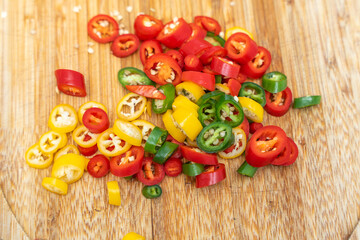 Assorted chopped chili peppers scattered on a wooden board. Vibrant colors emphasize freshness and spicy flavor.