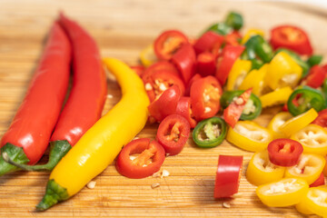 Whole red and yellow chili peppers beside sliced pieces on a wooden board. Fresh spicy ingredients ready for cooking.