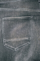 Close-up of a back pocket of black denim jeans highlighting stitching details. The texture and color create a stylish, urban aesthetic suitable for fashion marketing.