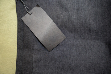 A black clothing tag attached to dark fabric, showcasing a minimalistic design on a smooth surface. This image is ideal for fashion marketing and retail advertising purposes.