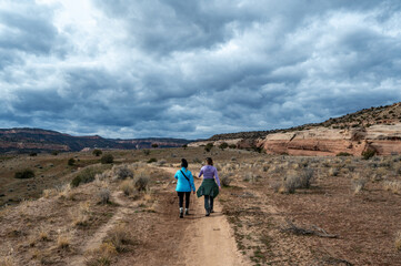 Fototapeta premium Two women hiking on Rustler's Loop trail near Loma, Colorado under stormy winter cloudscape.