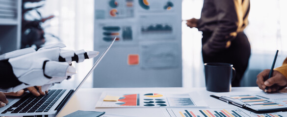 This image showcases a modern office environment where a robotic arm assists human workers in analyzing business data and charts, reflecting innovation and collaboration.Noogenesis