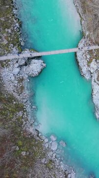 Breathtaking aerial footage of the emerald Soca river with a wooden footbridge in a rocky gorge. Slovenia.