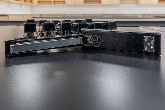 Close-up image of a open stapler on its side, with a organized group of staplers behind. 
