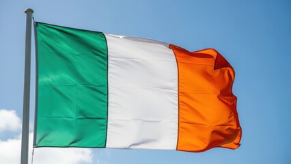 Obraz premium The flag of Ireland waving in the wind against a blue sky. Irish tricolor banner with green, white, and orange stripes. National symbol of the Republic of Ireland