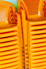 Stacked orange plastic chairs with patterned backs in bright outdoor setting
