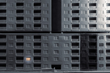 An empty high-rise panel house with one resident. An empty multi-story building with only one window with light at night. Abandoned city without people concept