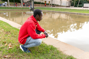 African man contemplating by pond in park, enjoying quiet travel moment