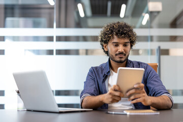 Young Indian man sitting at a desk in the office and using a tablet © Tetiana