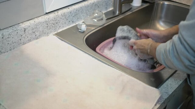 Medium shot of hands washing CPAP machine parts in soapy water at a kitchen sink, showing routine home cleaning and sleep apnea equipment maintenance. 15009  