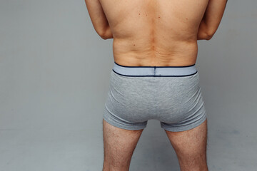 Obraz premium firm male ass in gray briefs. man standing with his back to the camera in underwear. concept: male health. loose skin on the lower back after diets and stress.