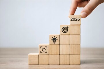 Hand placing a wooden block marked with the year 2026 atop a staircase representing achieving future business goals and objectives