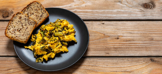 A plate with stir-fried bitter melon eggs and two pieces of bread on rustic wooden boards. Banner with copy space.