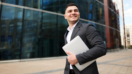 Businessman walks with laptop near modern building