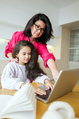 Mother helps daughter with laptop work at home