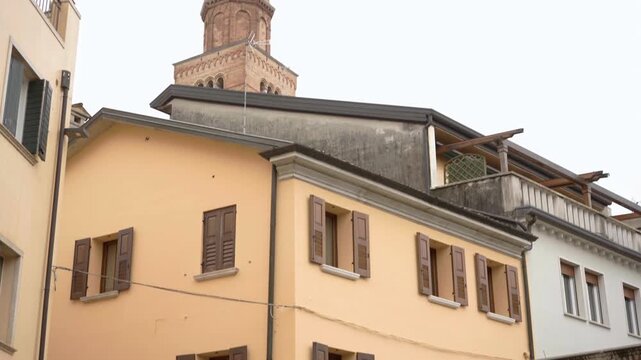 Brick bell tower of Duomo di San Marco rises above yellow houses with wooden shutters in historic center of Pordenone, Friuli-Venezia Giulia region, Italy.