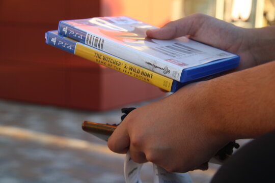 Close-up of a person holding two PS4 games: Batman: The Telltale Series and The Witcher 3: Wild Hunt - Game of the Year Edition. Gaming and lifestyle concept.