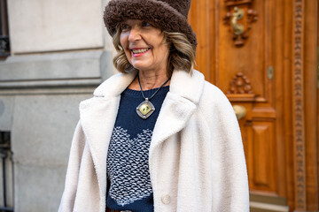Elegant woman in warm coat and stylish hat smiles joyfully on a chilly day in an urban setting