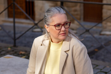 Elegant woman in a cream sweater and blazer reflects by an old stone building in a charming city, capturing the essence of quiet moments