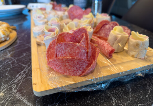 Close-up of creative salami rose and tortilla pinwheels on a wooden charcuterie board