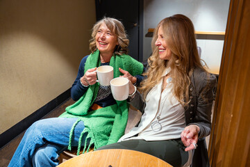 Two friends enjoy warm drinks and laughter in a cozy cafe setting during a rainy afternoon