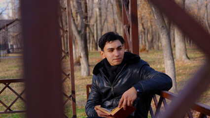 Young man reading an open book on a park bench.