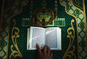A detailed macro shot of an open Quran with gold-leaf pages and Indonesian translation, illuminated by soft natural light on a traditional green prayer rug for religious study
