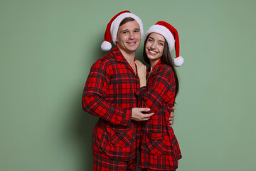 Fototapeta premium Happy couple in Santa hats and pajamas on greyish green background. Christmas atmosphere