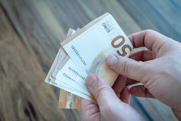Close up of male hands counting a stack of fifty euro banknotes over a wooden table representing savings and income