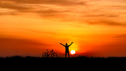 Silhouette of a person and a bike silhouetted against a beautiful sunset