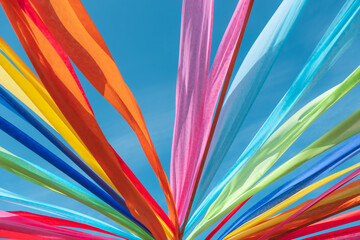 Vibrant multi colored fabric strips and ribbons blowing in the wind against a clear blue sky creating an abstract pattern