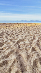 A sunny beach with textured sand stretches under a clear blue sky, inviting relaxation and exploration. The gentle waves of the sea appear in the background, a perfect day for travel