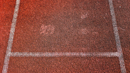 A close-up shot of a textured running track surface, with lane markings and hints of footprints
