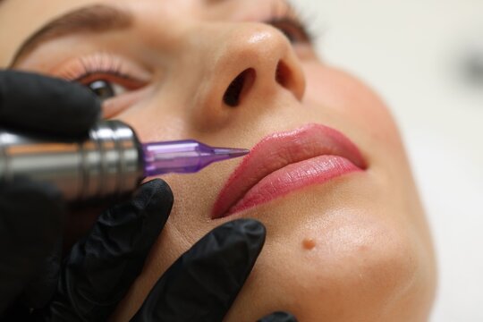 Beautician making permanent lip makeup to young woman, closeup