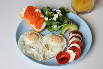 Healthy breakfast with fried eggs, salmon toast, avocado salad and juice