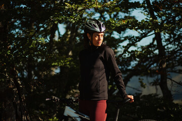 Portrait of a sporty girl with her bike in the forest, wearing a safety helmet