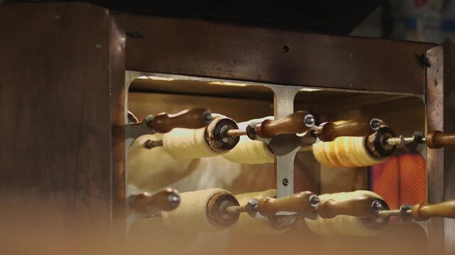 Traditional Baumstriezel baking at the Medieval Christmas Market on Wittelsbacherplatz, Muenchen. Authentic German pastry on wooden spits at the Munchner Adventsspektakel. Bavarian festive food