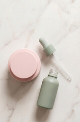 Minimal skincare set with dropper bottle and cream jar on marble background