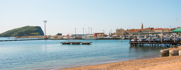 Pier with boats and mountain backdrop, banner. Coastal serenity, water transport, and scenic summer view in Budva, Montenegro.
