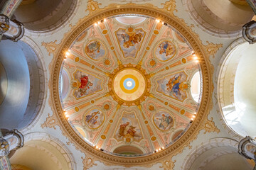 Naklejka premium The interior of Frauenkirche shows the dome with painted artworks. The structure features arches and columns. Visitors admire the beautiful ceiling design and historical details.