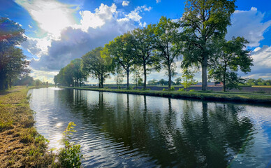 A beautiful, serene view of a tranquil canal lined with vibrant, lush trees beneath a clear, bright blue sky